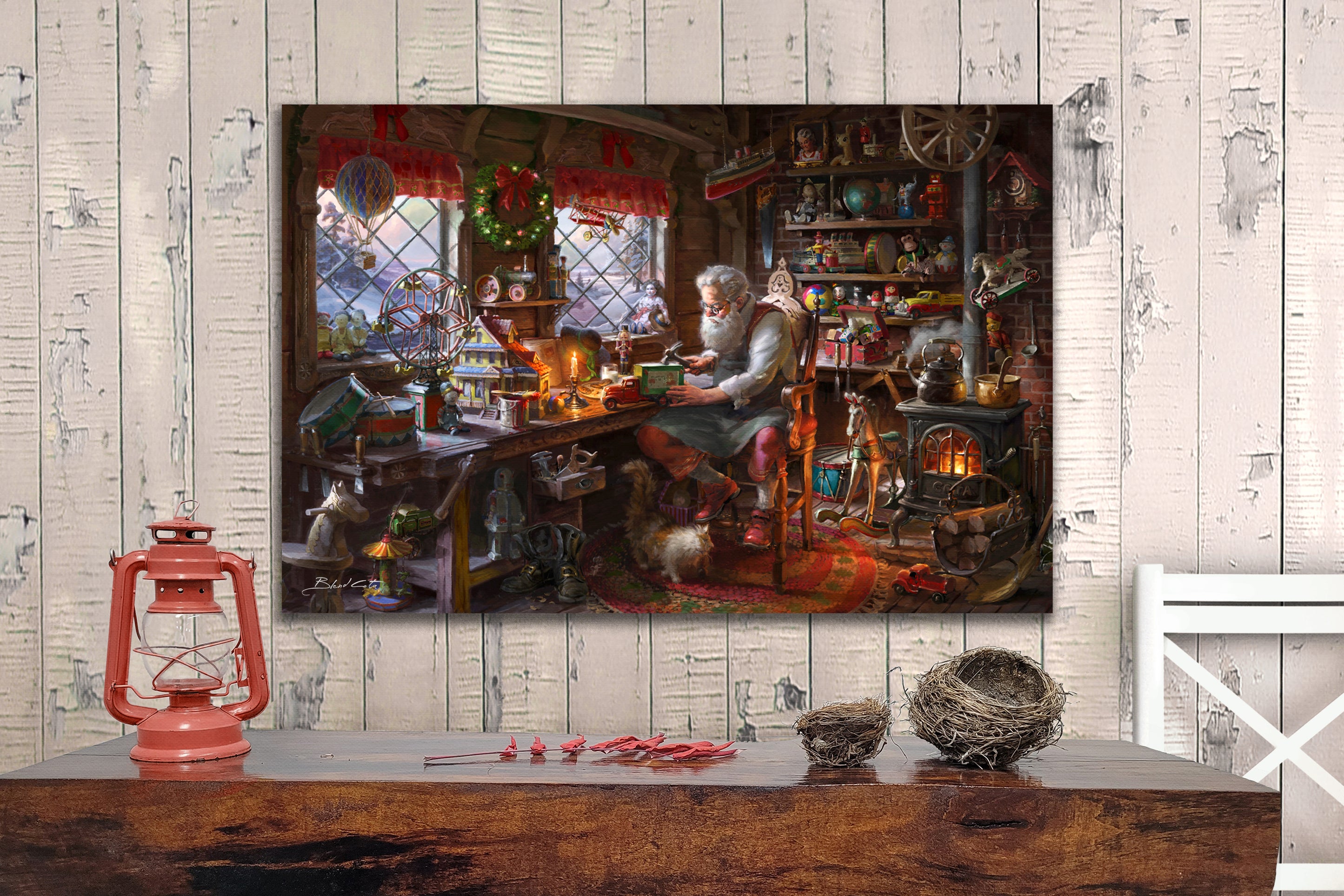 An original oil painting of Santa claus making toys in his workshop  during christmas with a cat by his boots and wood burning stove amongst the many children's toys in a room setting with white barn wood and fireplace. 